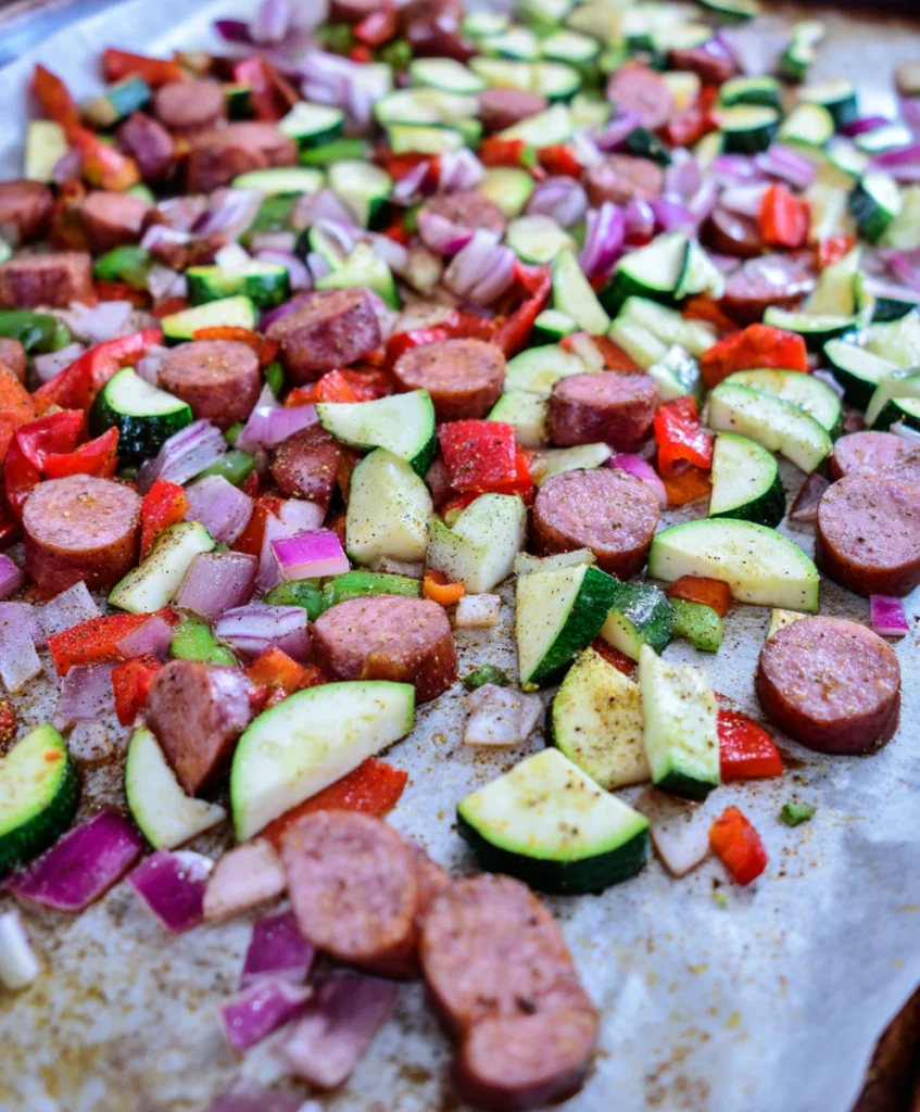 Easy One-Pan Cajun Sausage and Veggie Bake: Your New Weeknight Favorite! 2 Ingredients for One-Pan Cajun Sausage and Veggie Bake, including sausage, peppers, onions, and zucchini, seasoned on a baking sheet.